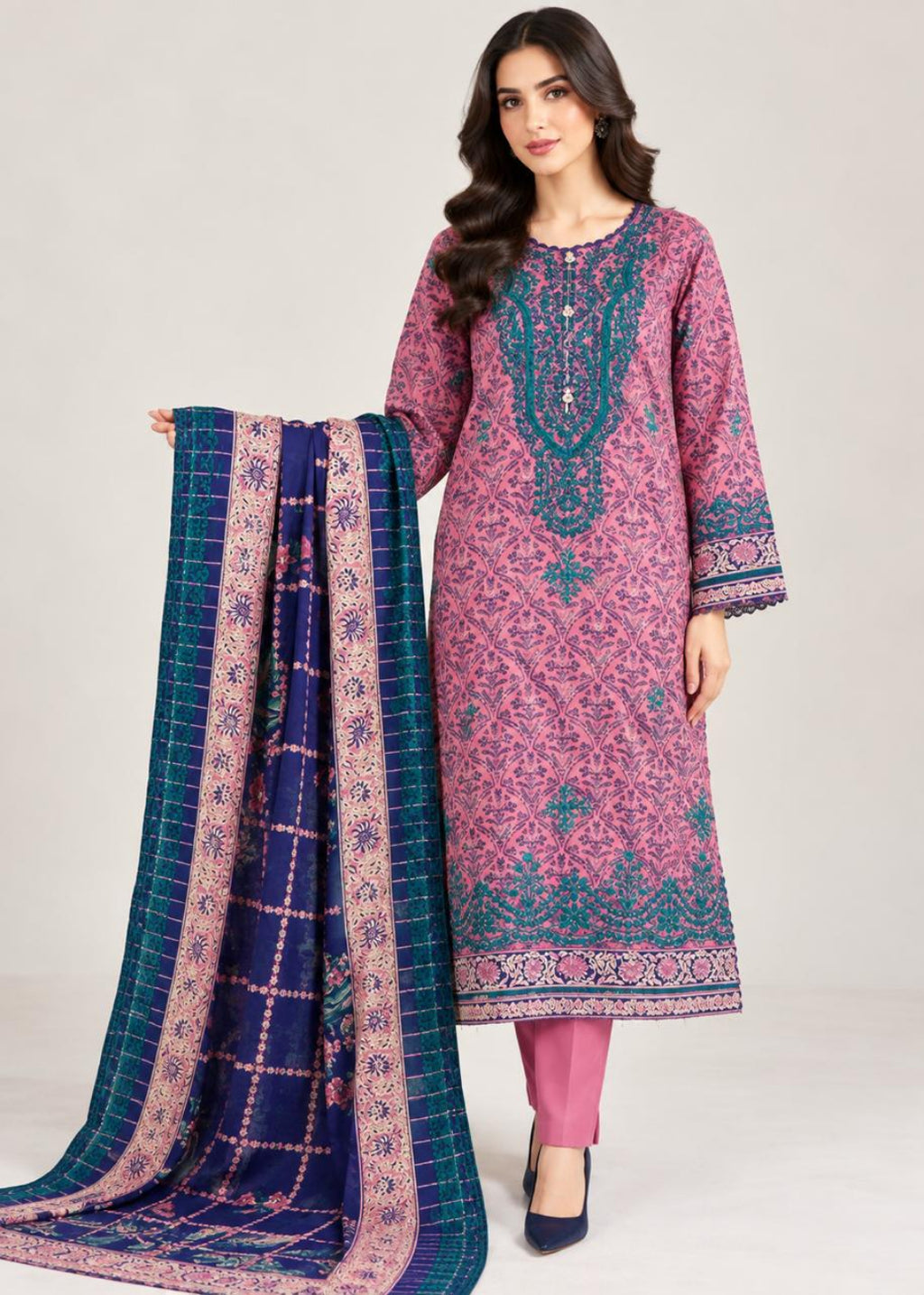 A woman models a traditional three-piece salwar kameez suit. The kurta is a dusty pink with teal and purple floral prints and heavy embroidery on the chest.