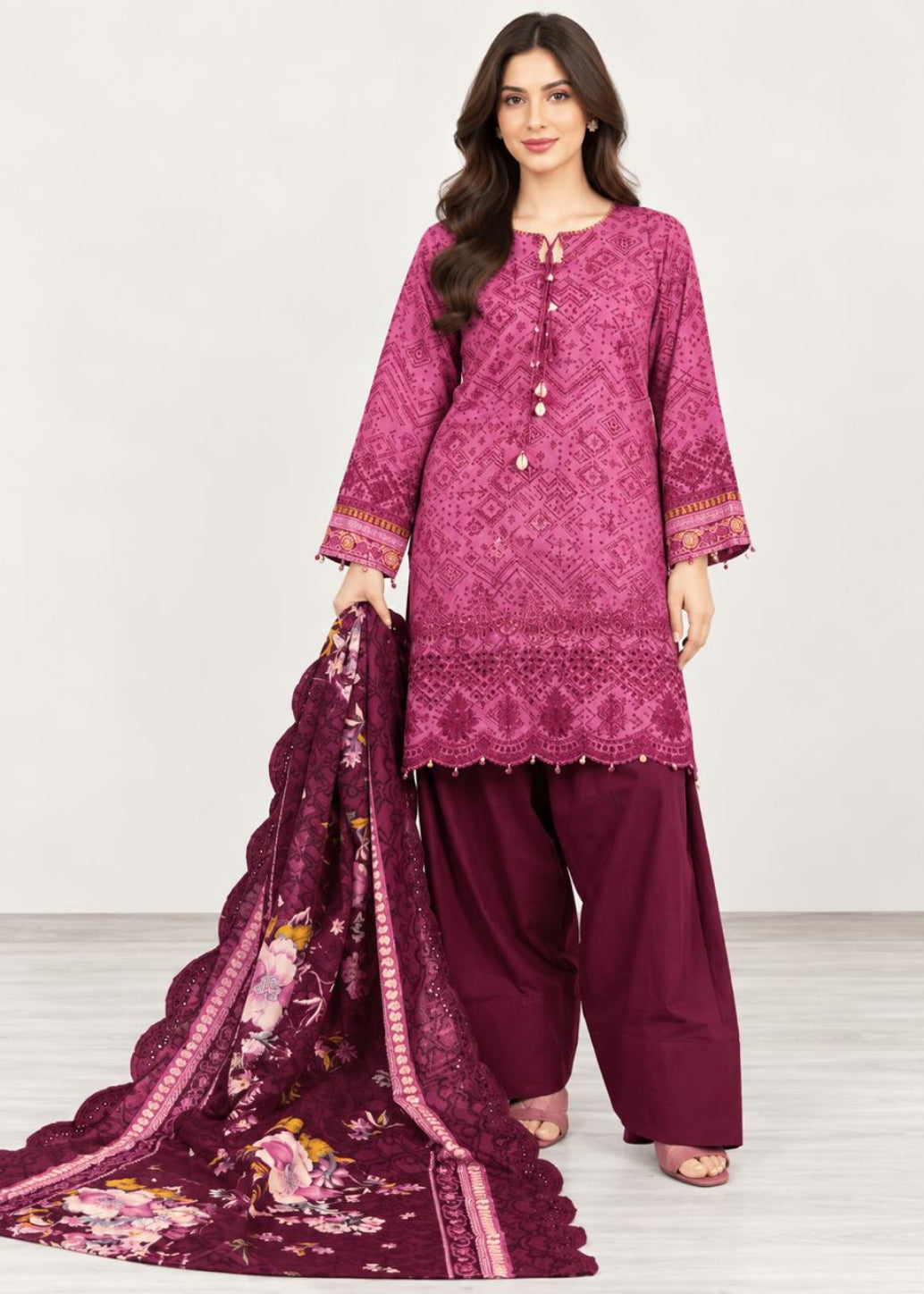 A woman modeling a three-piece traditional outfit consisting of a magenta embroidered kurta, deep maroon wide-leg pants, and a matching deep maroon floral dupatta, set against a plain light gray studio background.