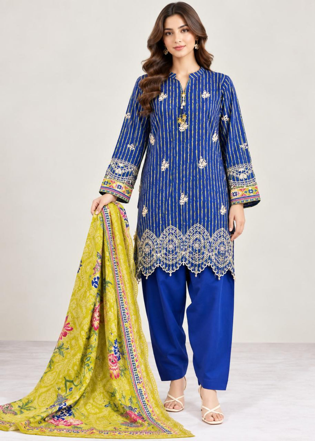 A woman models a traditional three-piece salwar kameez suit in royal blue and yellow. The kurta is royal blue with vertical gold stripes and intricate silver embroidery, paired with matching blue pants and a yellow floral dupatta with a blue border.