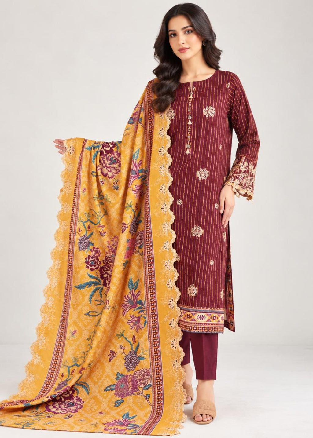 A woman models a traditional South Asian salwar kameez set featuring a deep maroon kurta with vertical stripes and gold embroidery, paired with maroon pants and a bright yellow printed dupatta.