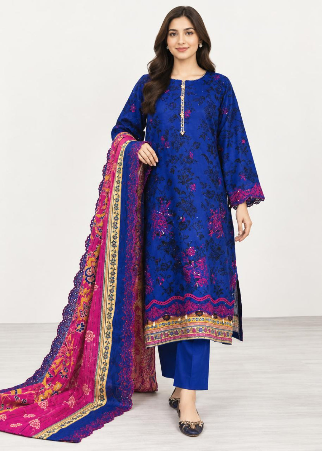 A woman modeling a royal blue embroidered kurta set with a matching pink and blue dupatta, featuring intricate floral embroidery and gold zari detailing.