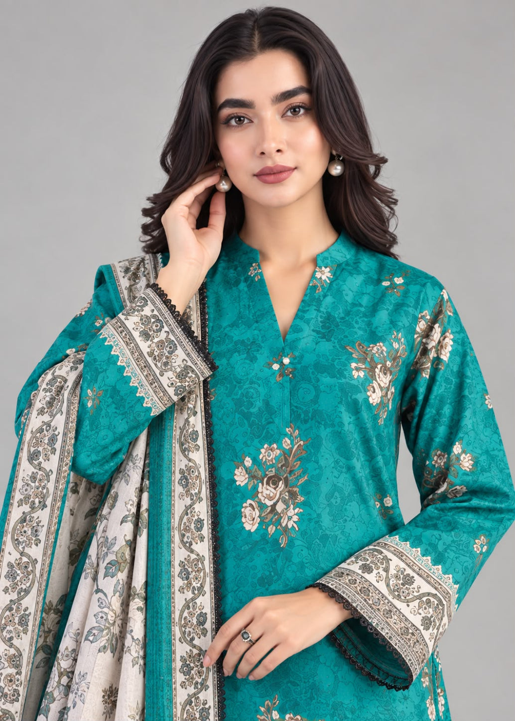 A woman modeling a teal green embroidered kurta with a matching dupatta. The kurta features intricate floral embroidery in gold, beige, and white, with patterned cuffs.
