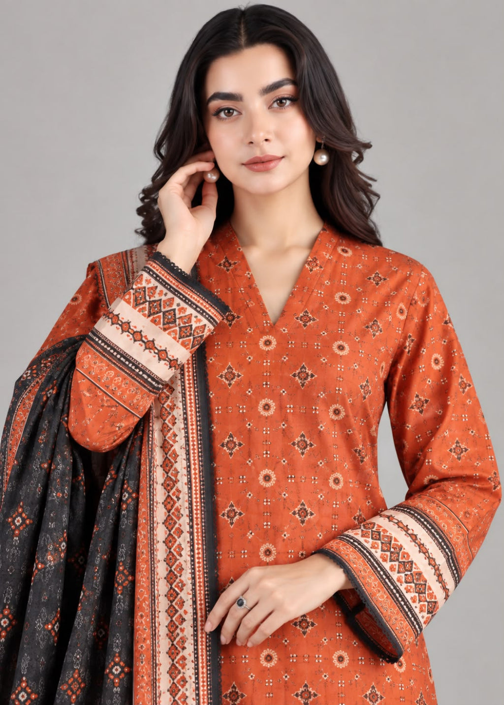 A woman modeling a traditional South Asian salwar kameez set in rust orange with a black dupatta featuring intricate geometric patterns and a matching orange border print.
