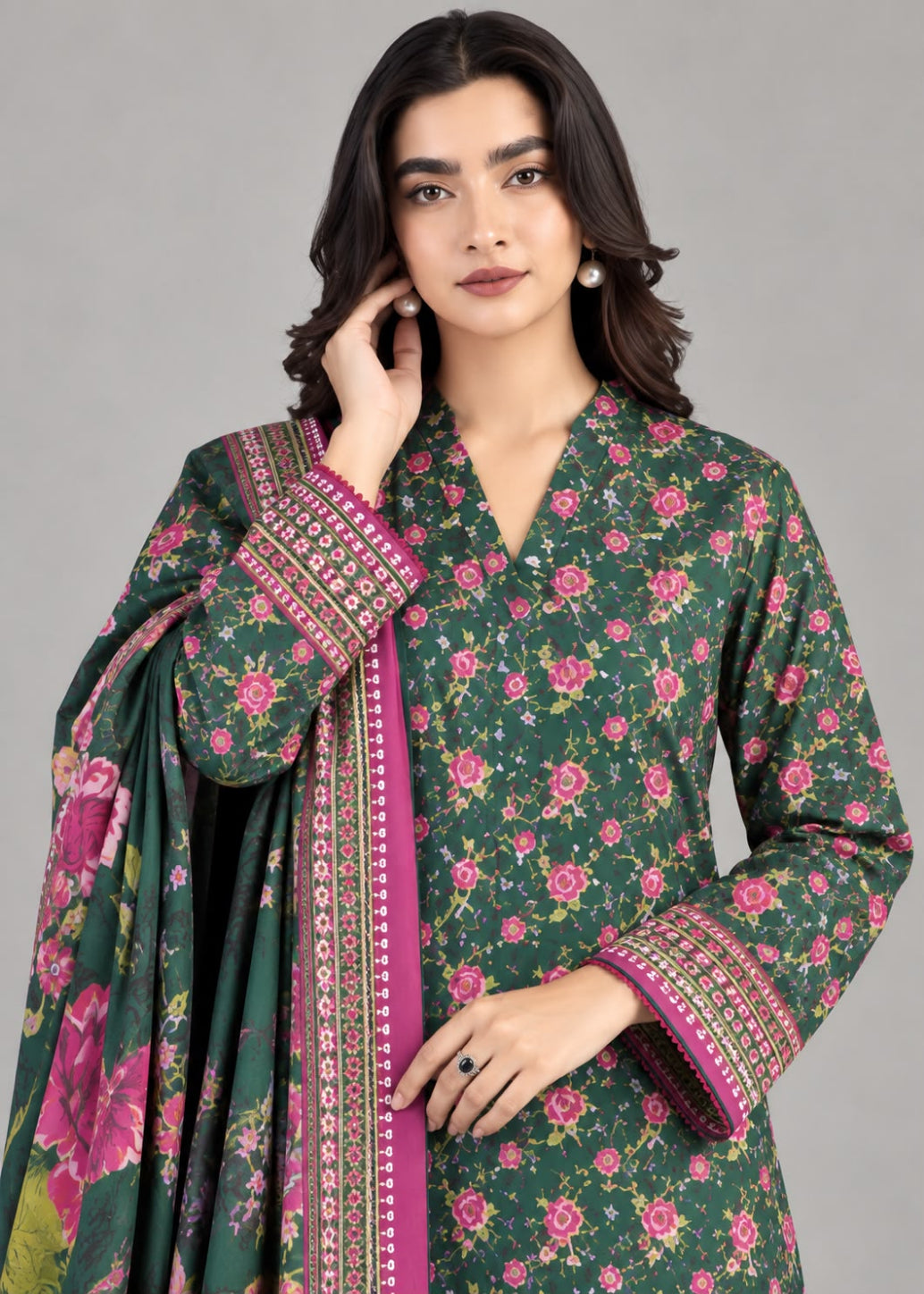 A woman modeling a dark green floral salwar kameez suit with pink and magenta borders, paired with a matching floral dupatta, against a solid gray studio background.