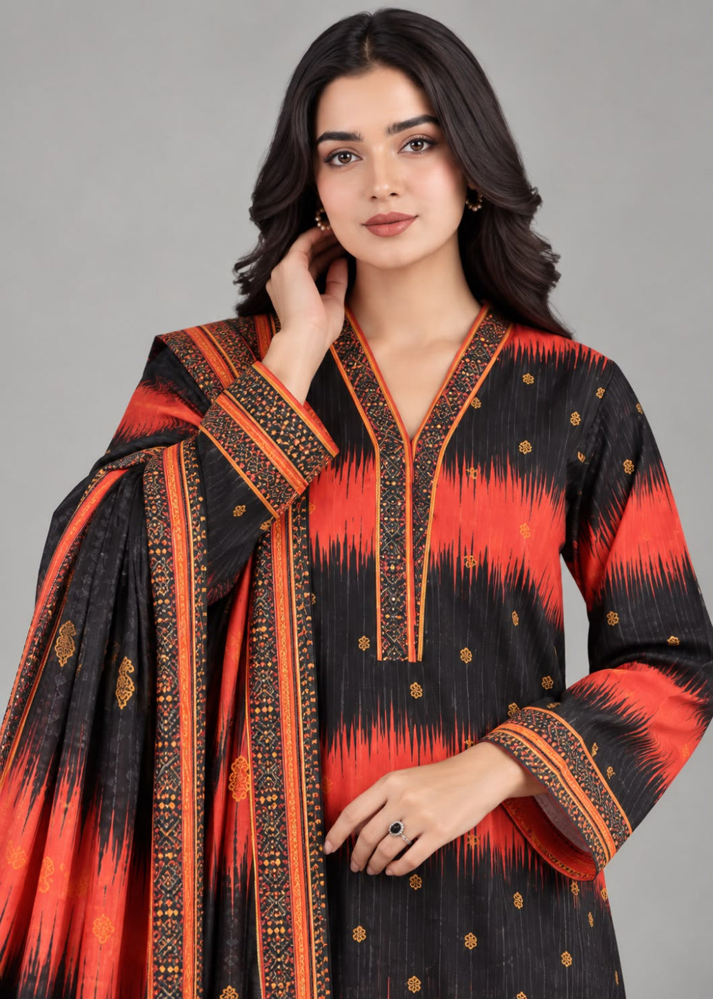 A woman modeling a black and orange printed ethnic kurta set with a matching dupatta, featuring orange ikat-like patterns and gold embroidered details, set against a solid gray studio background.