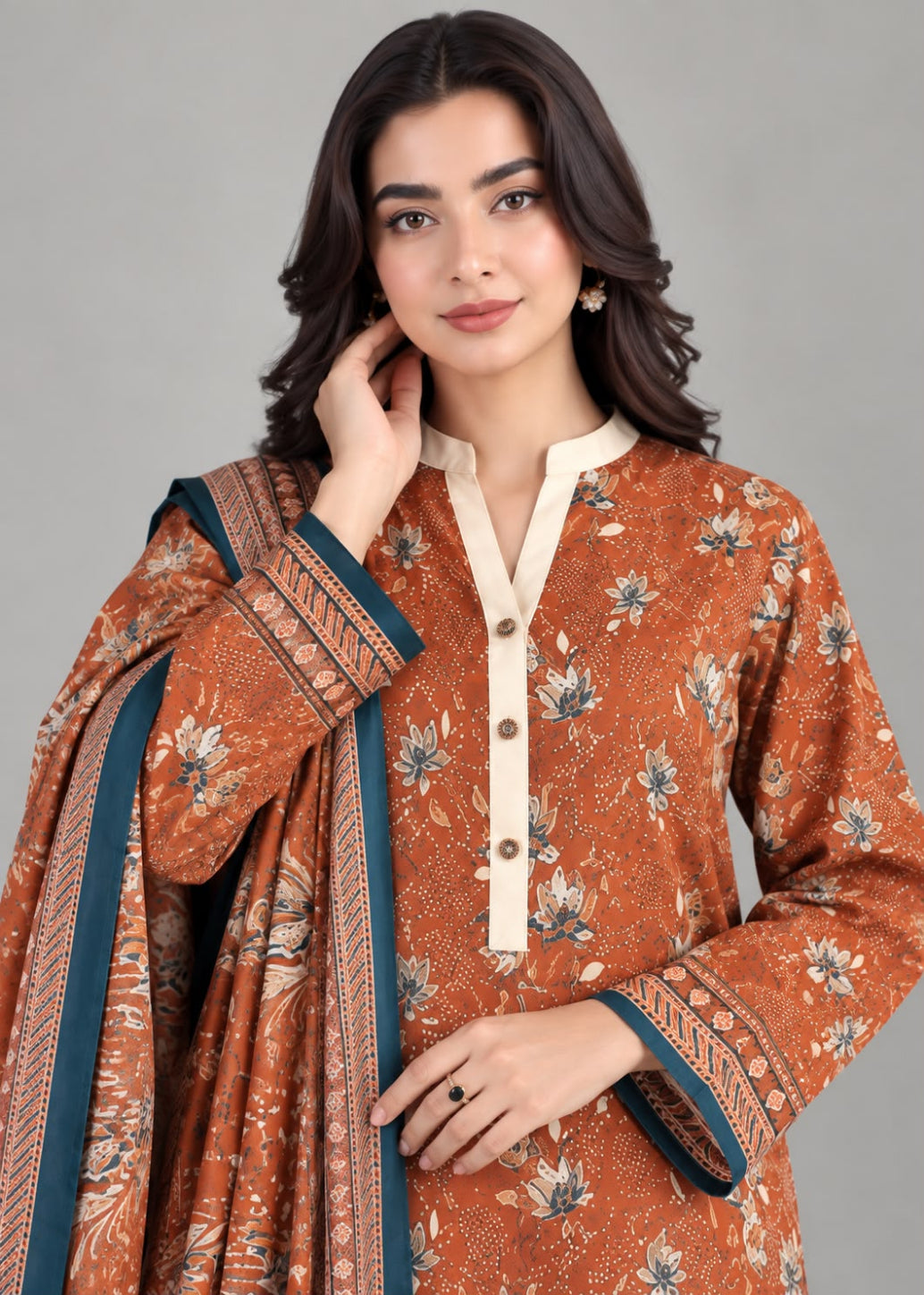 A woman modeling a rust-orange printed kurta with a cream mandarin collar and button placket, paired with a matching dupatta featuring teal and cream borders, against a solid gray studio background.