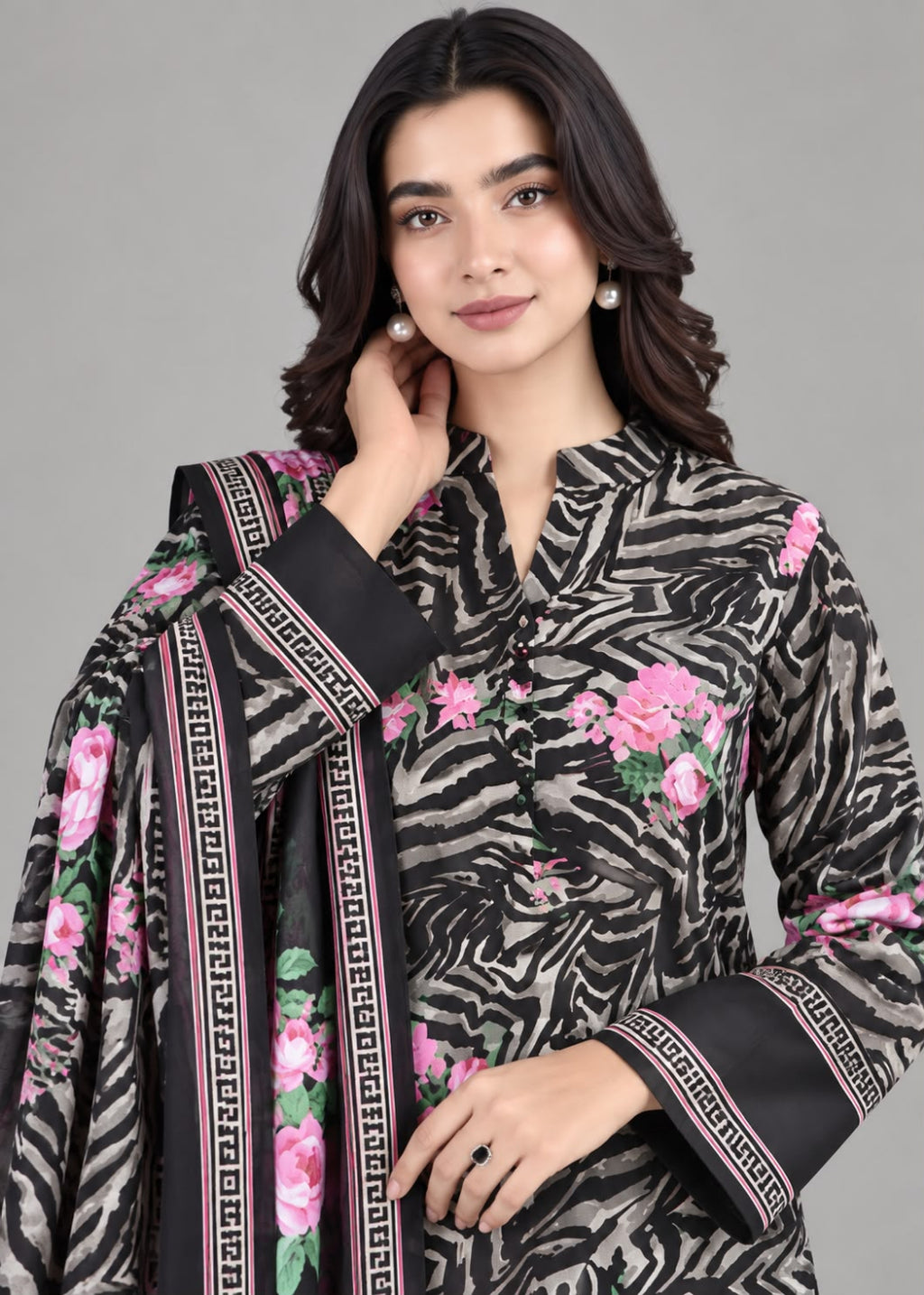 A woman modeling a black and gray zebra-print three-piece suit with pink floral embroidery and a matching dupatta with a pink and black Greek key border, set against a solid gray background.