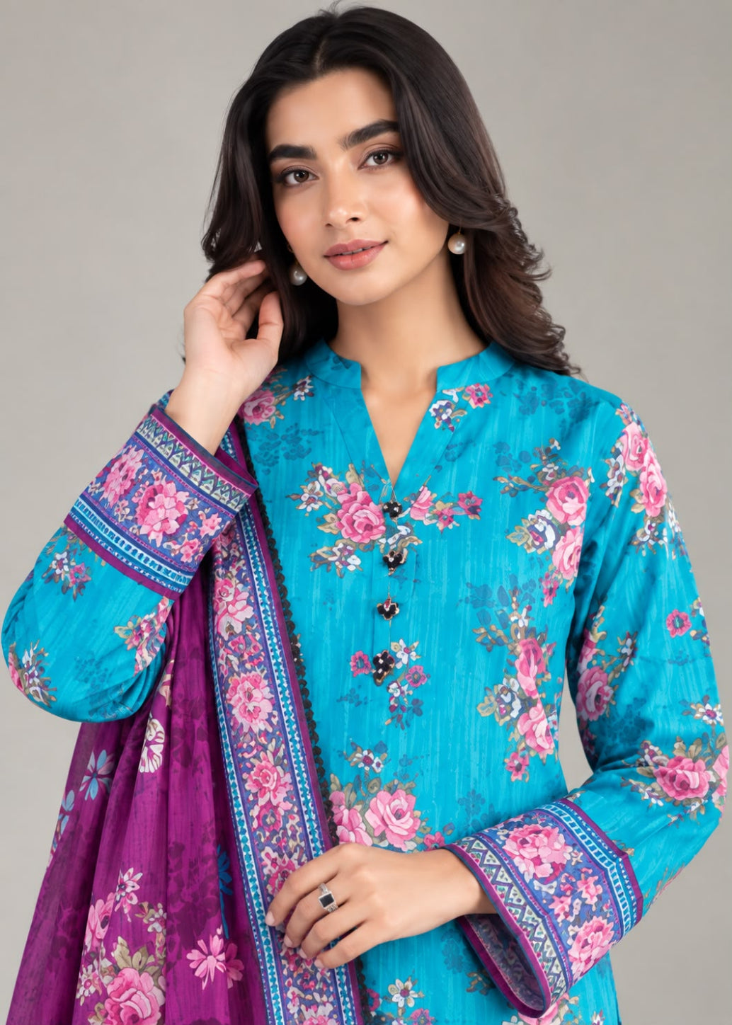 A woman modeling a vibrant turquoise blue floral printed kurta with a matching purple dupatta, set against a solid light gray studio background.