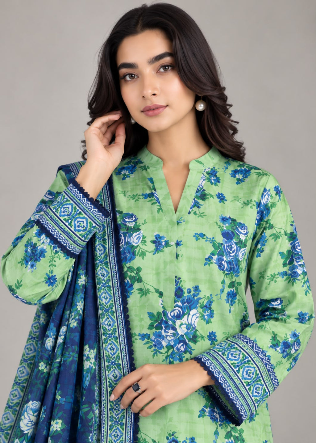 A woman modeling a light green three-piece ethnic suit with a blue floral print and matching dupatta, featuring a mandarin collar and patterned cuffs.