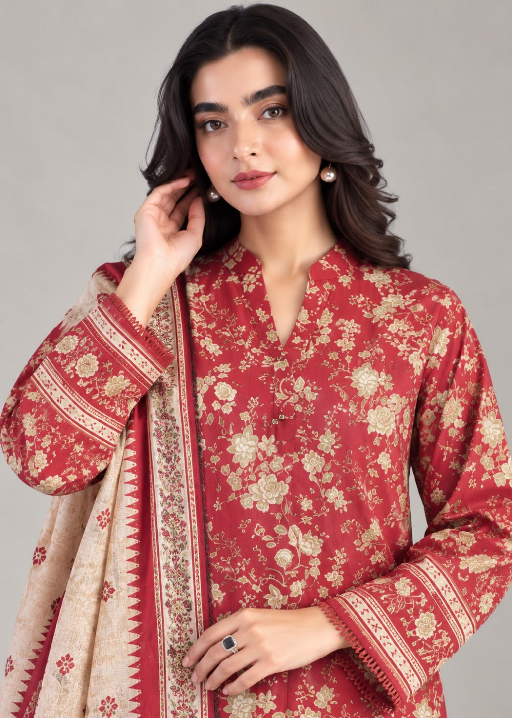 A woman modeling a red floral printed kurta with a beige dupatta featuring red and gold borders, set against a solid gray studio background.