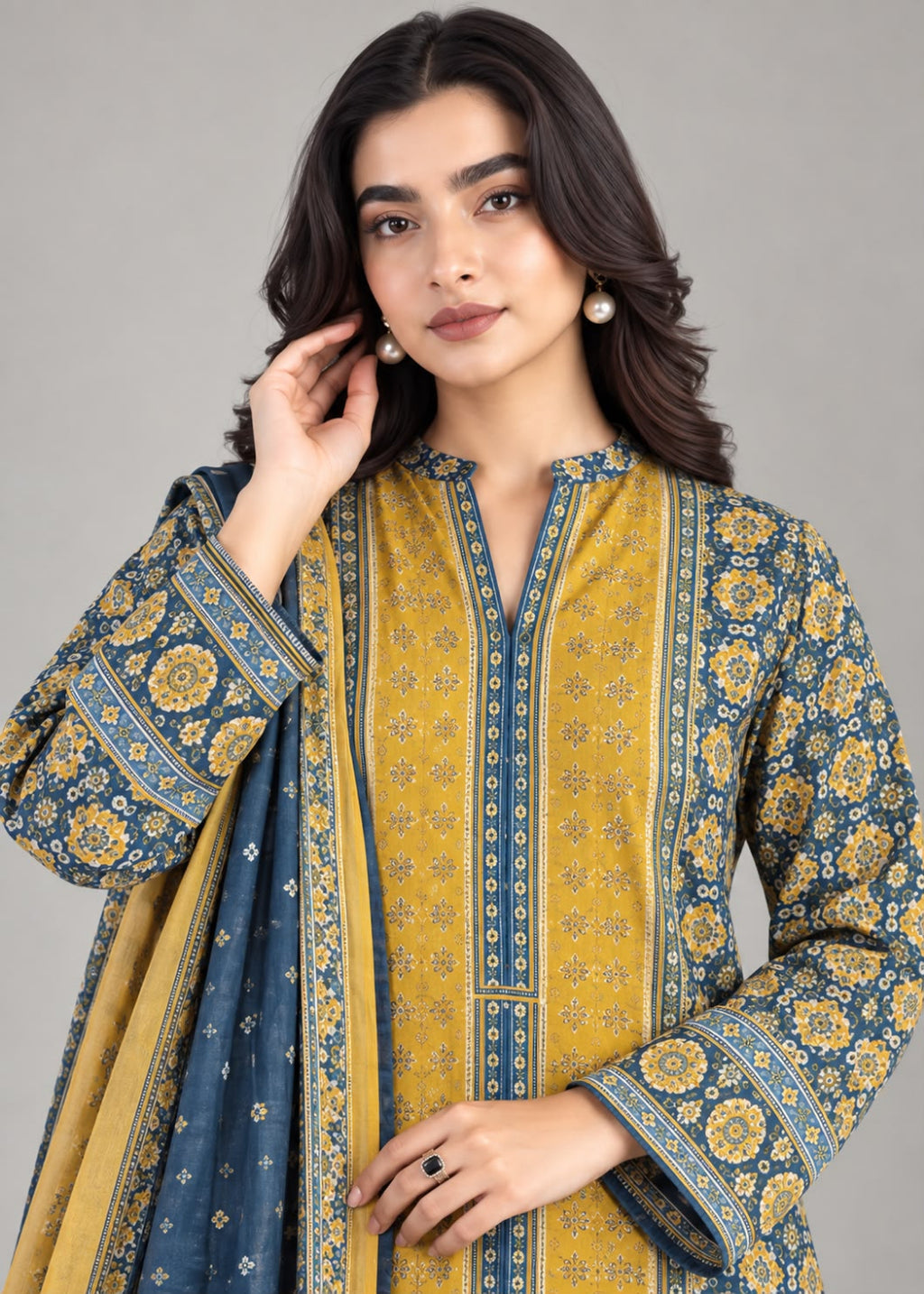 A woman modeling a traditional three-piece salwar kameez set in mustard yellow and navy blue with intricate floral block prints and borders, paired with a matching navy dupatta.