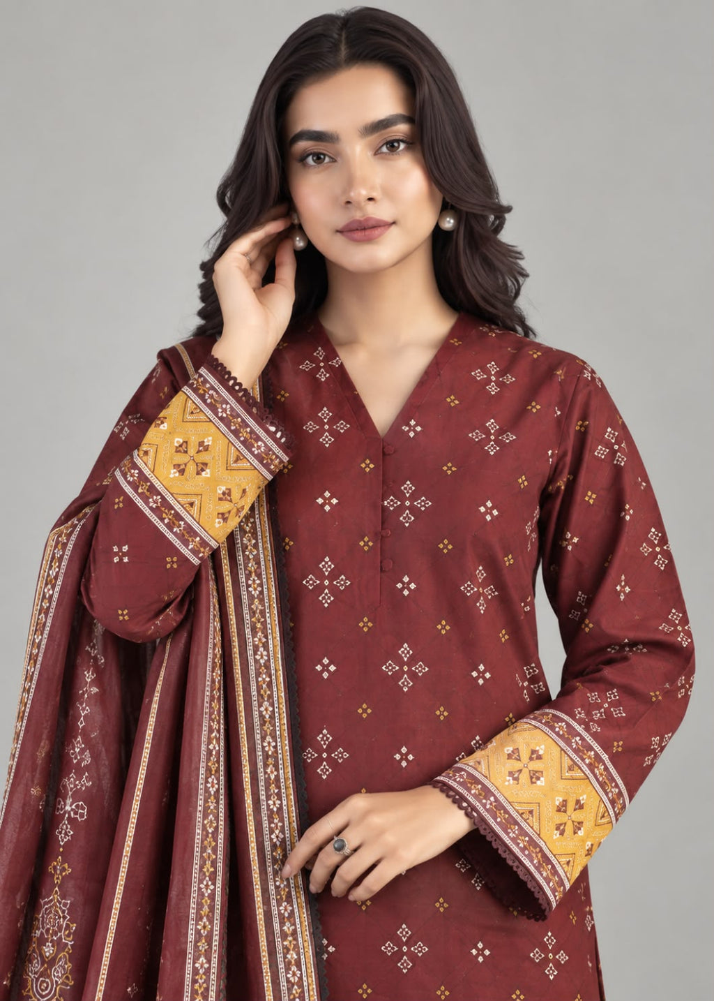 A woman modeling a traditional three-piece salwar kameez suit in maroon. The kurta features small white and gold geometric prints, with wide yellow and maroon patterned cuffs.