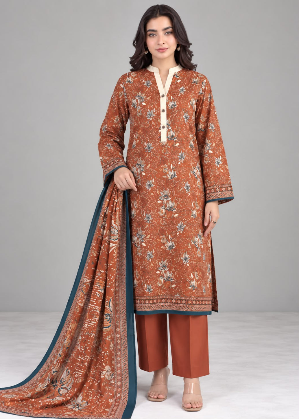 A woman models a rust-orange printed salwar kameez suit with a matching dupatta, paired with rust-orange trousers, against a neutral gray studio background.
