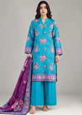 A woman models a traditional three-piece salwar kameez suit set. The set features a turquoise blue printed kurta with pink floral motifs and a purple border, matching wide-leg trousers in turquoise, and a purple dupatta with pink floral prints and a blue border.