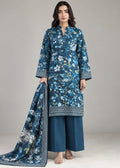 A woman models a three-piece traditional Indian salwar kameez suit set in a studio setting. The set features a blue floral printed kurta with white and light blue floral motifs and a geometric border, paired with solid blue wide-leg trousers and a matching printed dupatta.