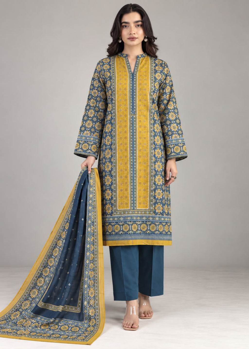 A woman models a traditional three-piece salwar kameez suit set. The set features a mustard yellow and navy blue printed kurta with a matching navy blue dupatta, paired with navy blue trousers, against a neutral gray studio background.