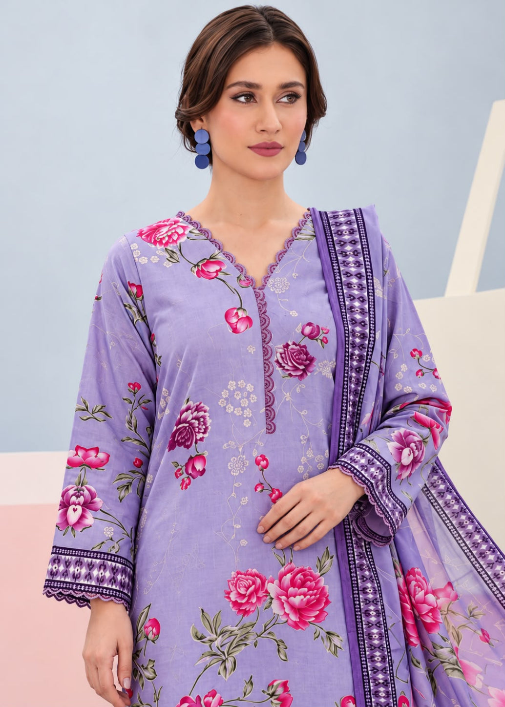 A woman modeling a lavender purple floral printed kurta with a matching printed dupatta. The kurta features pink rose prints, green leaves, and a purple patterned border on the neckline, cuffs, and dupatta.