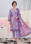 A woman models a three-piece lavender ethnic suit set featuring a floral printed kurta, matching trousers, and a sheer printed dupatta, set against a pastel studio background.