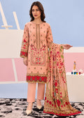 A woman models a peach-colored three-piece ethnic suit with intricate red and gold floral embroidery, paired with matching trousers and a coordinating dupatta, set against a pastel studio backdrop.