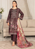 A woman models a three-piece traditional South Asian outfit consisting of a dark plum kurta with floral embroidery, matching trousers, and a large multicolored printed dupatta in a living room setting.