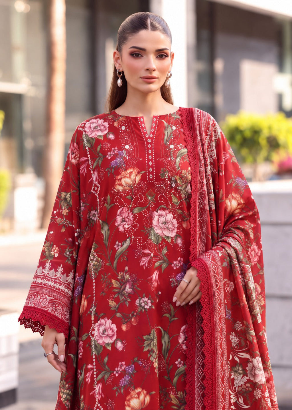 A woman modeling a red three-piece unstitched salwar kameez suit with a floral print and embroidered details, featuring a matching dupatta.