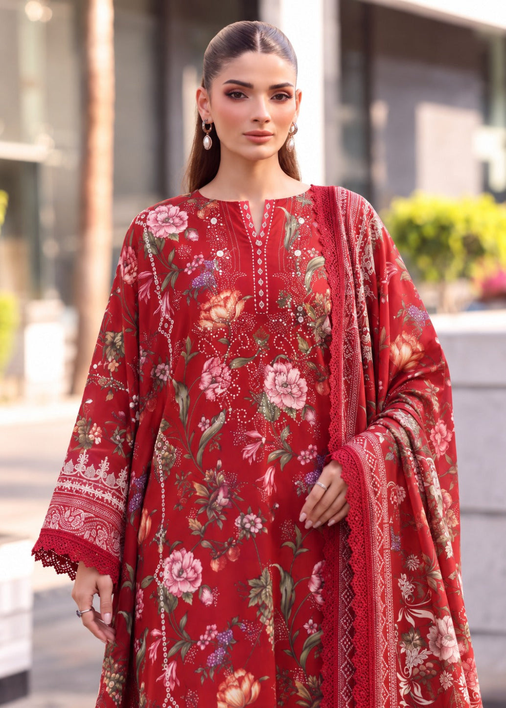 A woman modeling a red three-piece unstitched salwar kameez suit with a floral print and embroidered details, featuring a matching dupatta.