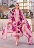 A woman models a three-piece pink ethnic suit with a vibrant magenta floral print, consisting of a long kurta, matching trousers, and a sheer dupatta, set against an outdoor urban background.