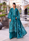 A woman stands outdoors in a plaza wearing a teal traditional outfit with matching pants and a sheer dupatta, featuring light blue floral embroidery and printed motifs.