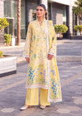 A woman models a light yellow three-piece traditional South Asian salwar suit set outdoors. The set includes a long kurta with blue and green floral embroidery and white lace trim, matching wide-leg trousers, and a coordinating dupatta.