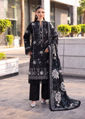 A woman models a black three-piece traditional outfit with intricate silver floral embroidery, featuring a long kurta, wide-leg trousers, and a matching dupatta, set against an outdoor urban background.