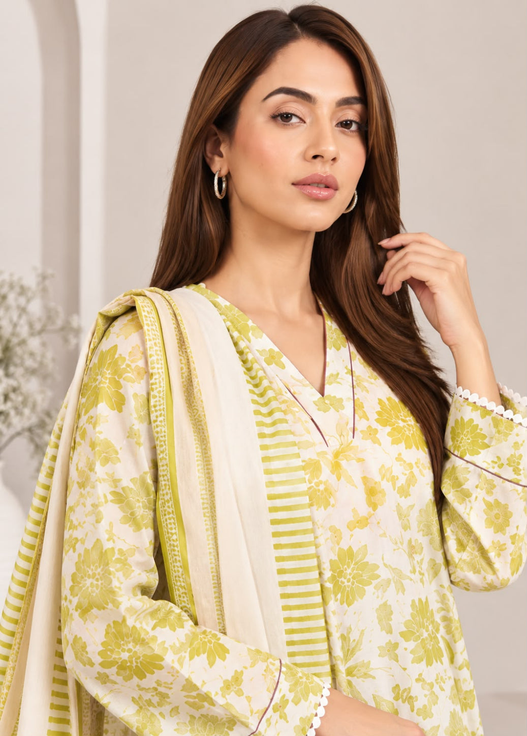 A woman modeling a traditional three-piece salwar kameez suit in a soft cream and olive green colorway. The outfit features a cream-colored kurta with an olive green floral print, matching olive green striped border details, and a coordinating cream dupatta with green borders.