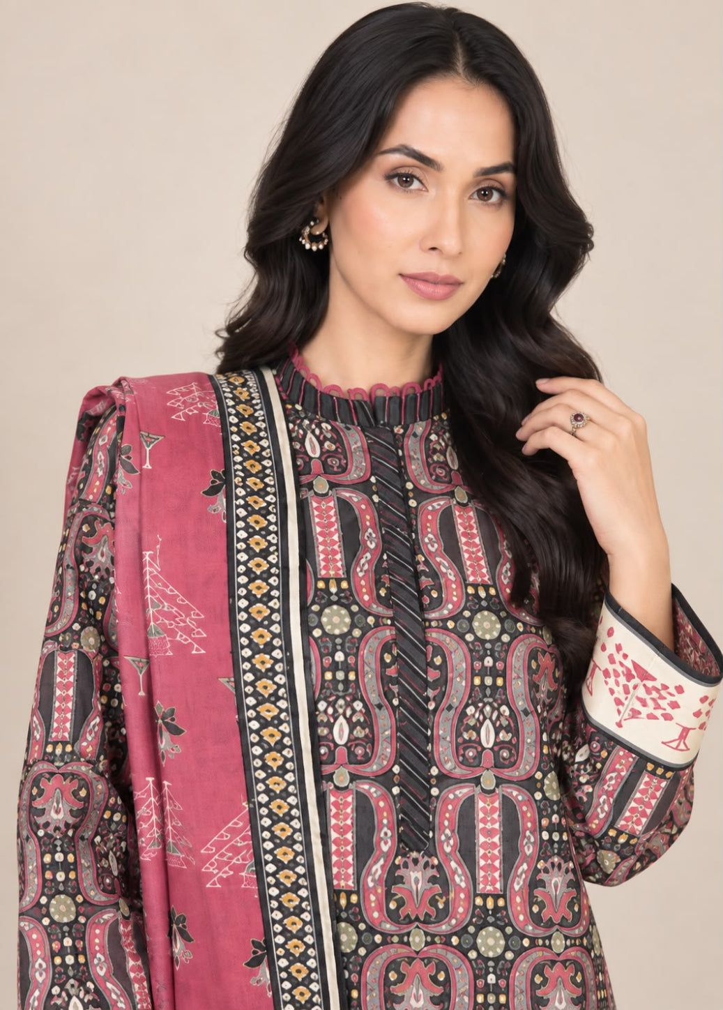 A woman modeling a traditional South Asian salwar kameez set featuring a pink dupatta and a black kurta with intricate red, beige, and gold paisley patterns.