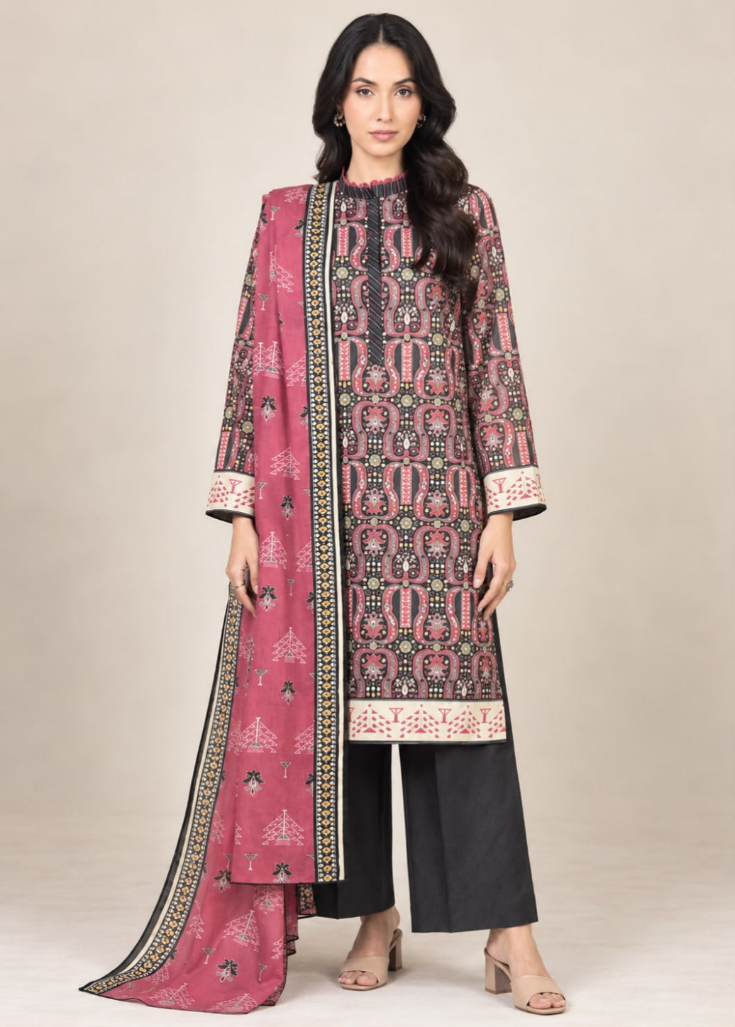 A woman modeling a traditional three-piece salwar kameez suit set. The set features a dusty pink printed kameez kurta with black and beige geometric patterns, black wide-leg trousers, and a matching pink printed dupatta with a black border.