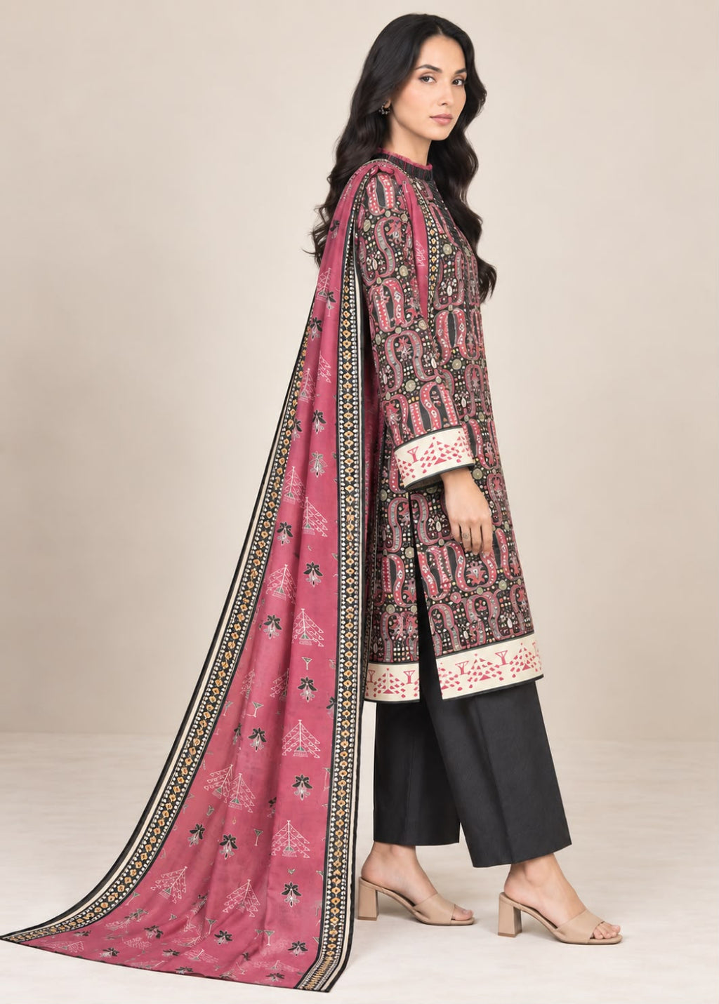 A woman modeling a traditional Indian salwar kameez suit. The outfit features a dusty pink printed kameez kurta with black and white patterns, black pants, and a matching pink printed dupatta with a black border, set against a plain beige background.