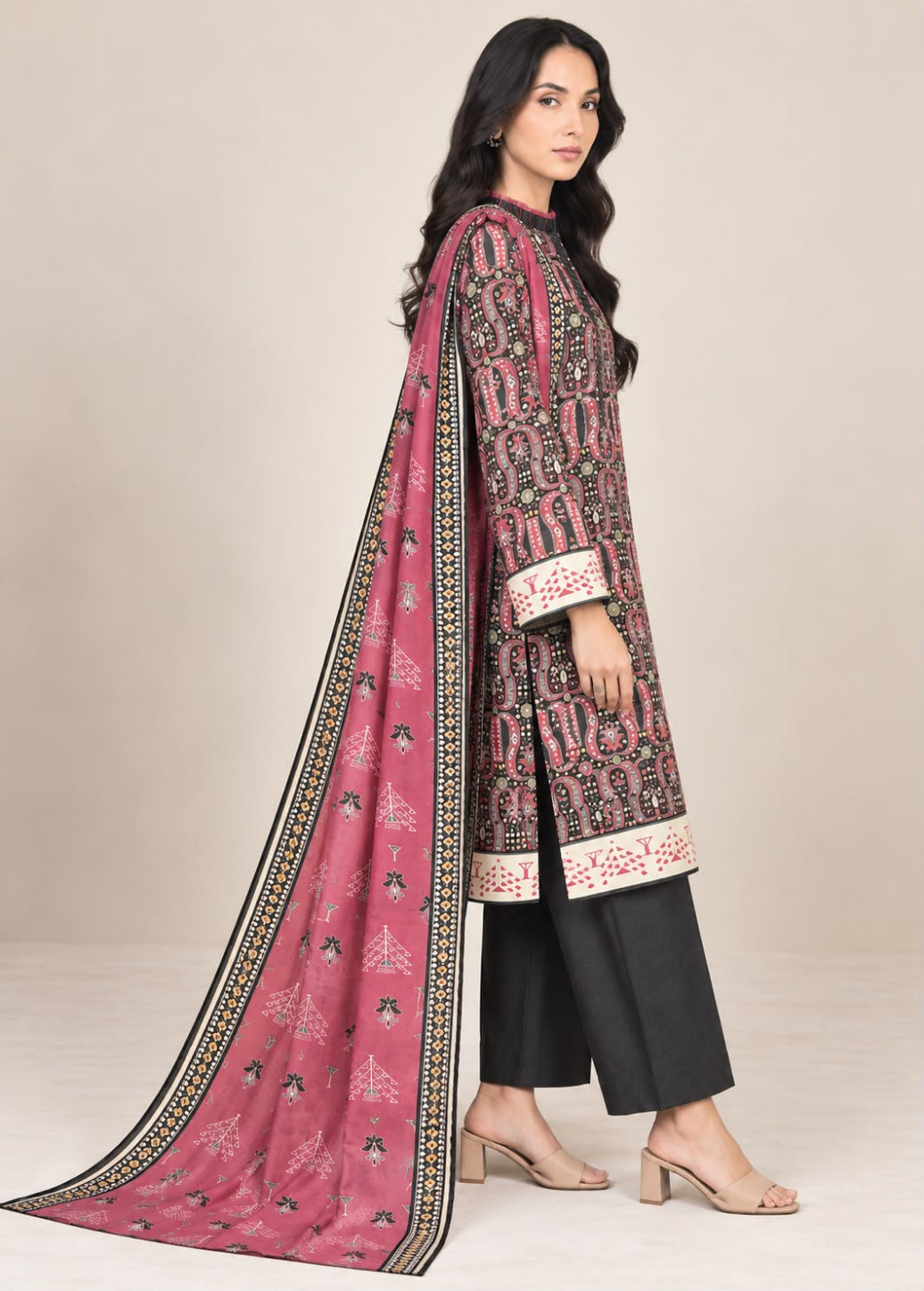 A woman modeling a traditional Indian salwar kameez suit. The outfit features a dusty pink printed kameez kurta with black and white patterns, black pants, and a matching pink printed dupatta with a black border, set against a plain beige background.