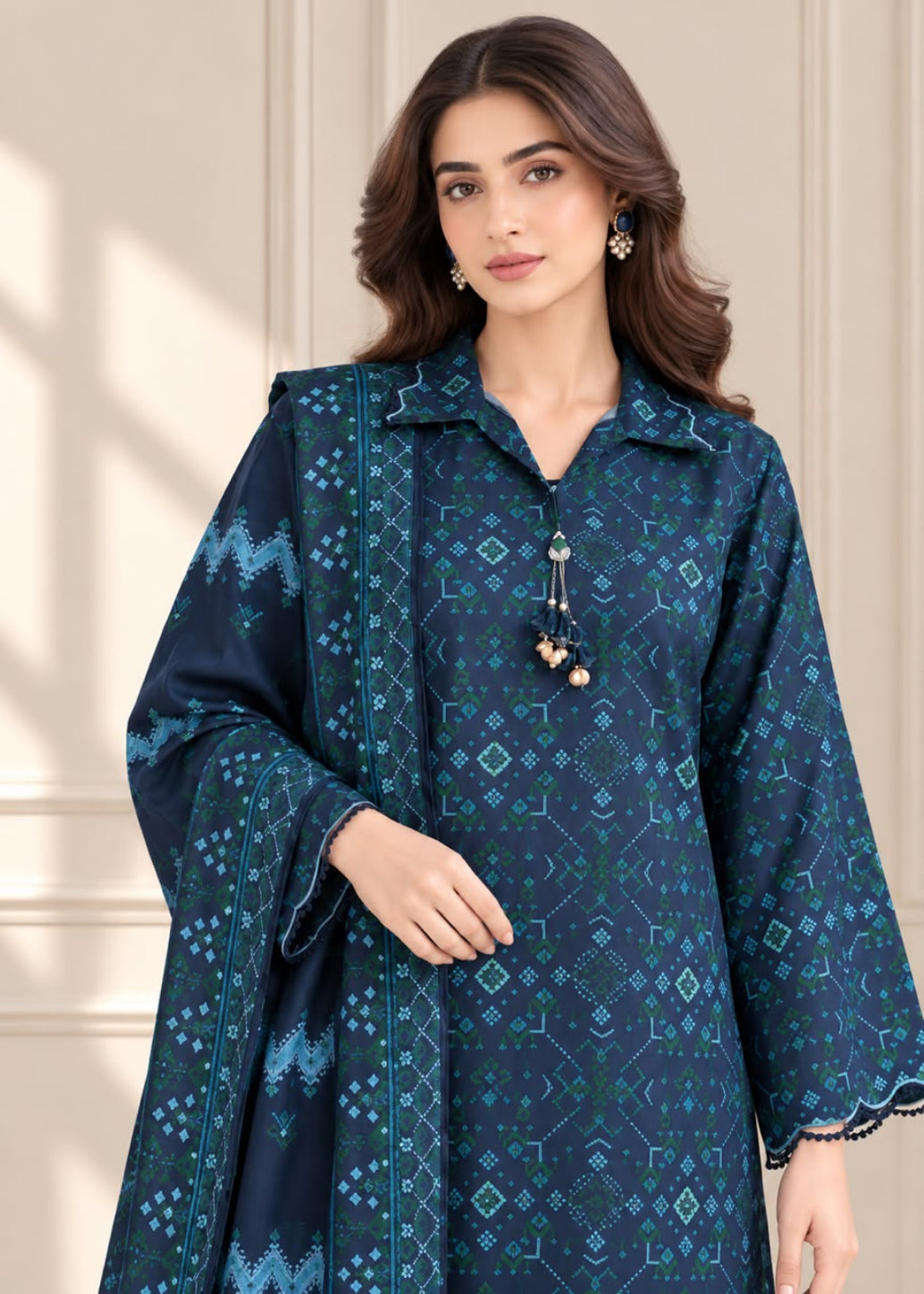 A woman modeling a dark teal blue printed kurta with matching patterned dupatta, featuring geometric and tribal patterns, set against a neutral beige paneled wall.