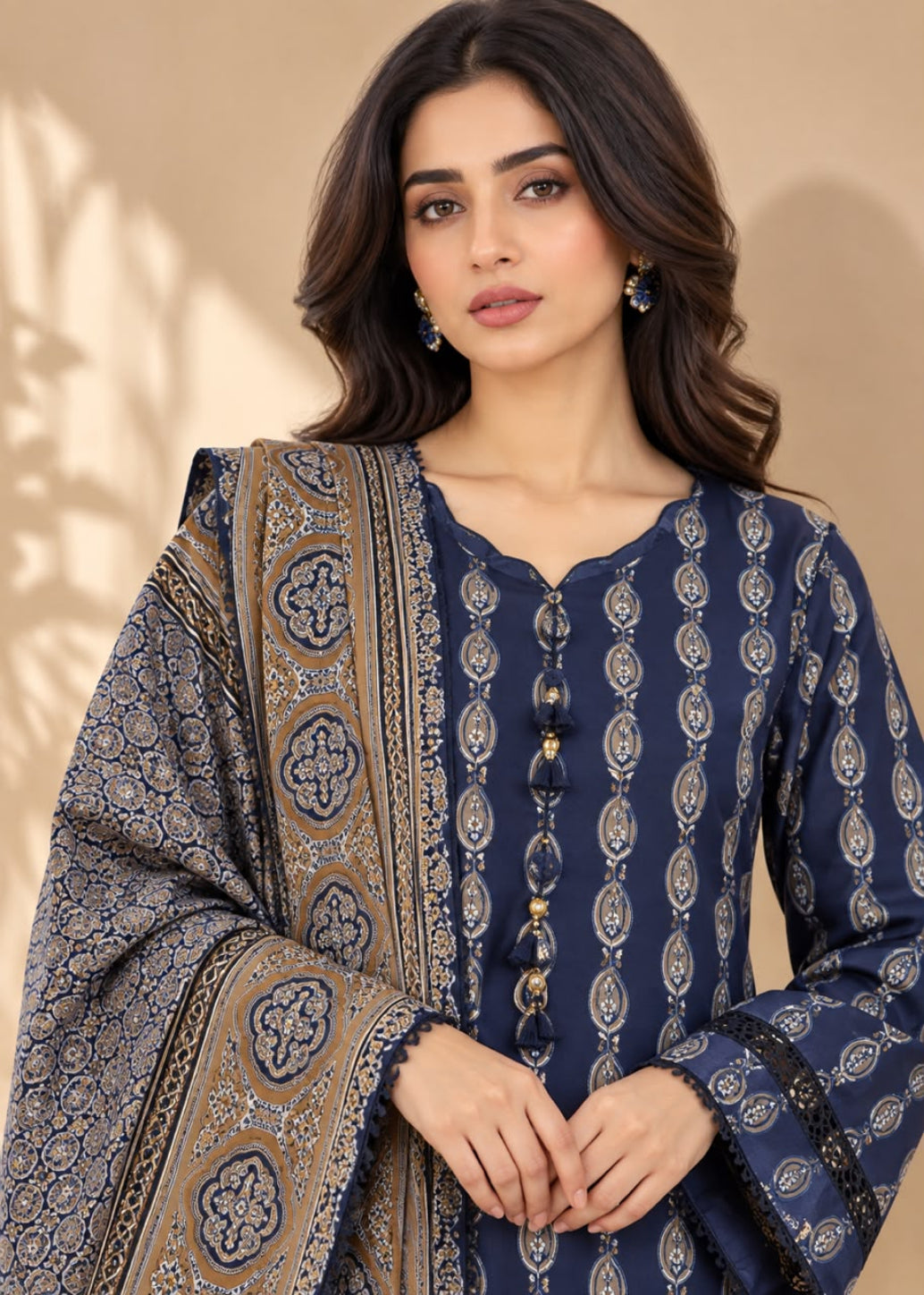 A woman modeling a navy blue printed kurta with a matching patterned dupatta, set against a warm beige background with soft leaf shadows.