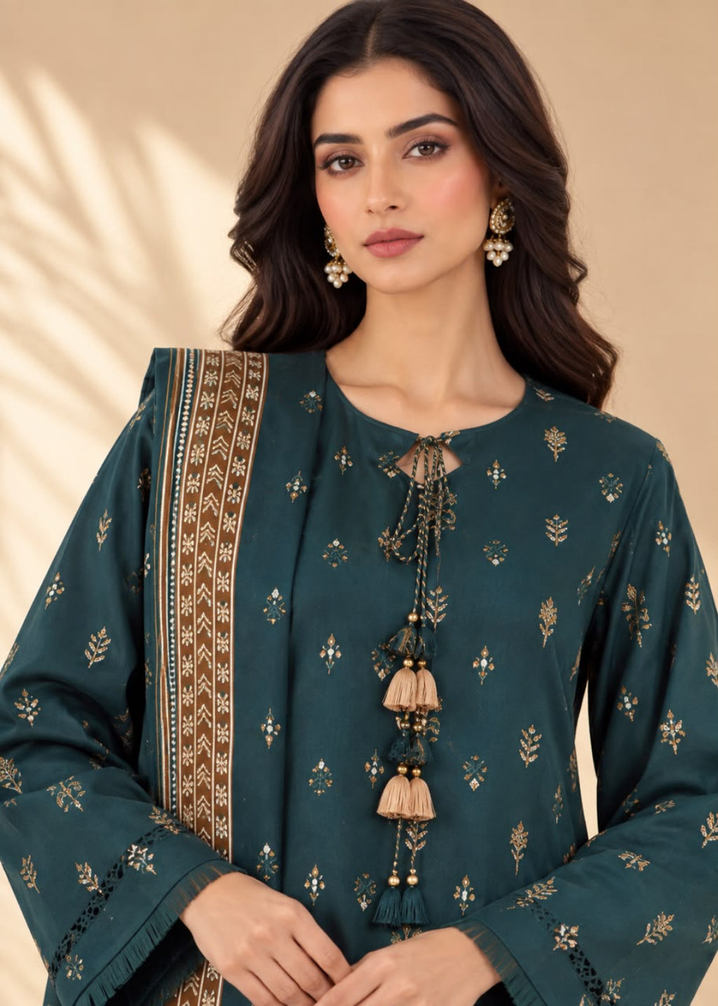 A woman modeling a dark teal green kurta with gold floral prints, a matching patterned dupatta, and decorative tassel ties at the neckline, set against a warm beige background.