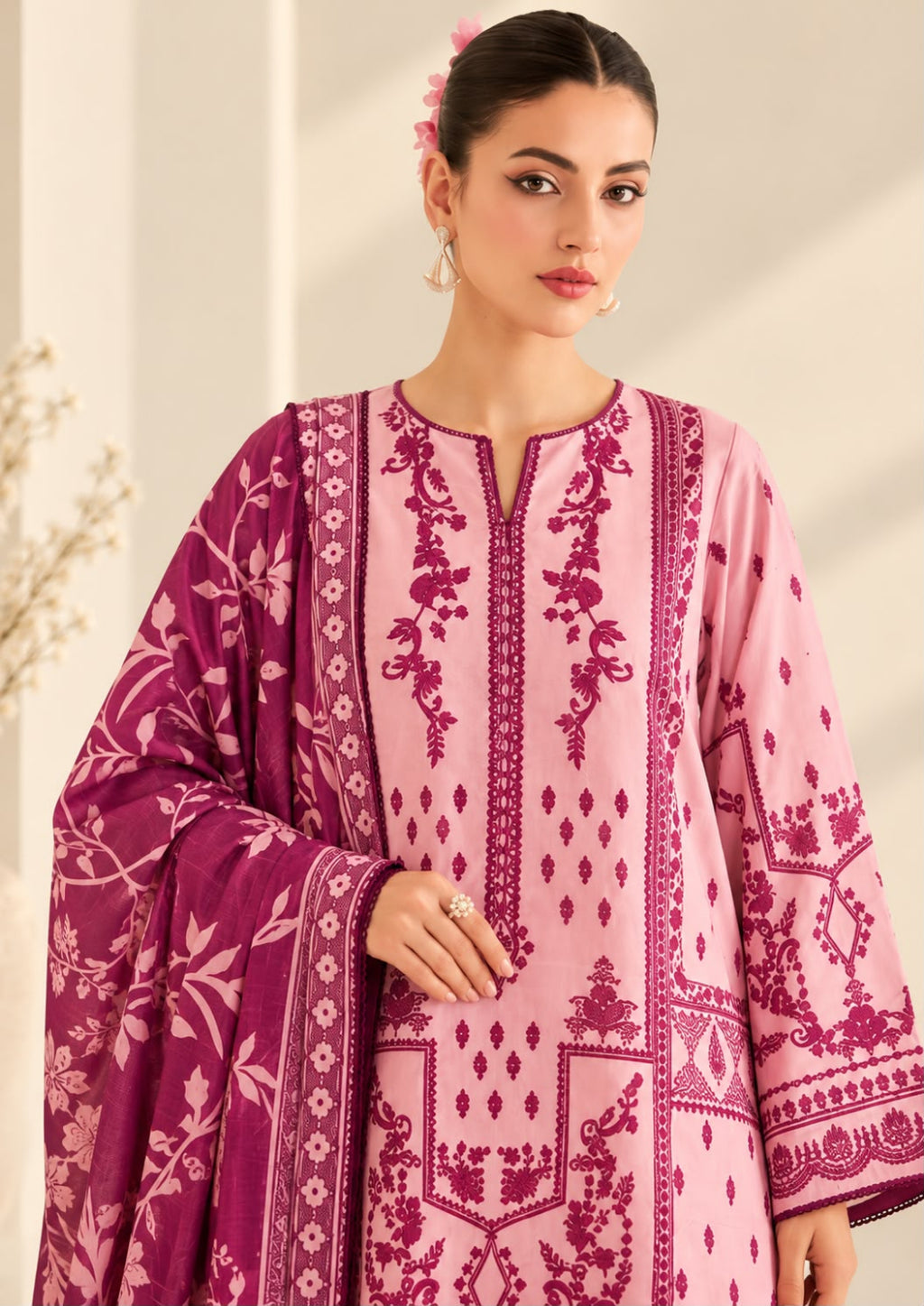 A woman modeling a pink traditional kurta with magenta embroidery and a matching patterned dupatta, set against a softly lit beige background.