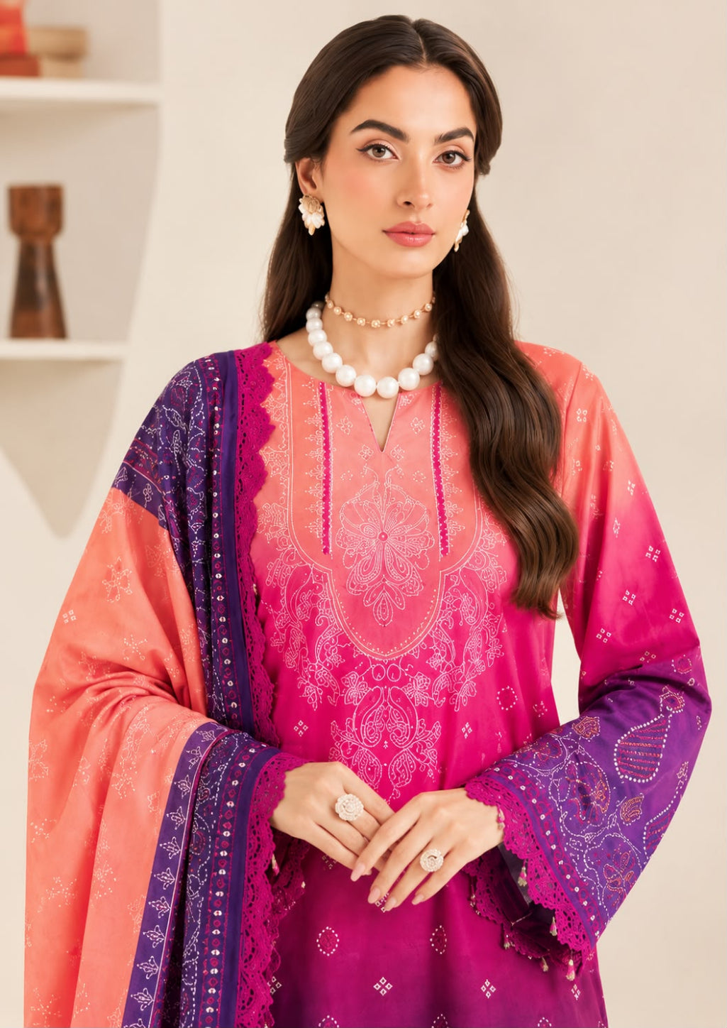 A woman modeling a traditional South Asian salwar kameez set featuring a vibrant pink and magenta embroidered kurta with a matching purple dupatta, styled with a pearl necklace and earrings.