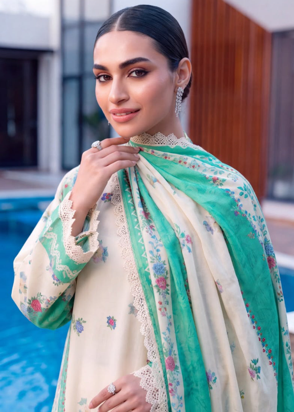A woman modeling a traditional South Asian outfit in a split-screen lifestyle setting with a swimming pool and modern building in the background. The outfit consists of a cream-colored embroidered kurta, matching wide-leg trousers, and a vibrant green dupatta with floral patterns and lace borders.