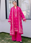A woman modeling a bright pink traditional outfit with matching printed dupatta and wide-leg trousers, standing outdoors in front of a white wall and window.