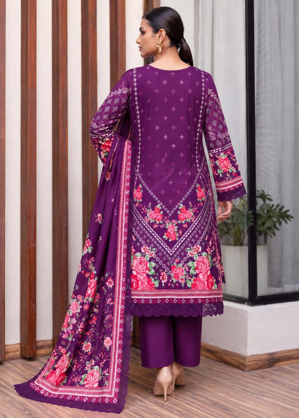 A woman wearing a purple ethnic three-piece suit with pink and red floral embroidery, shown from the back in an indoor setting with wooden paneling and a window.