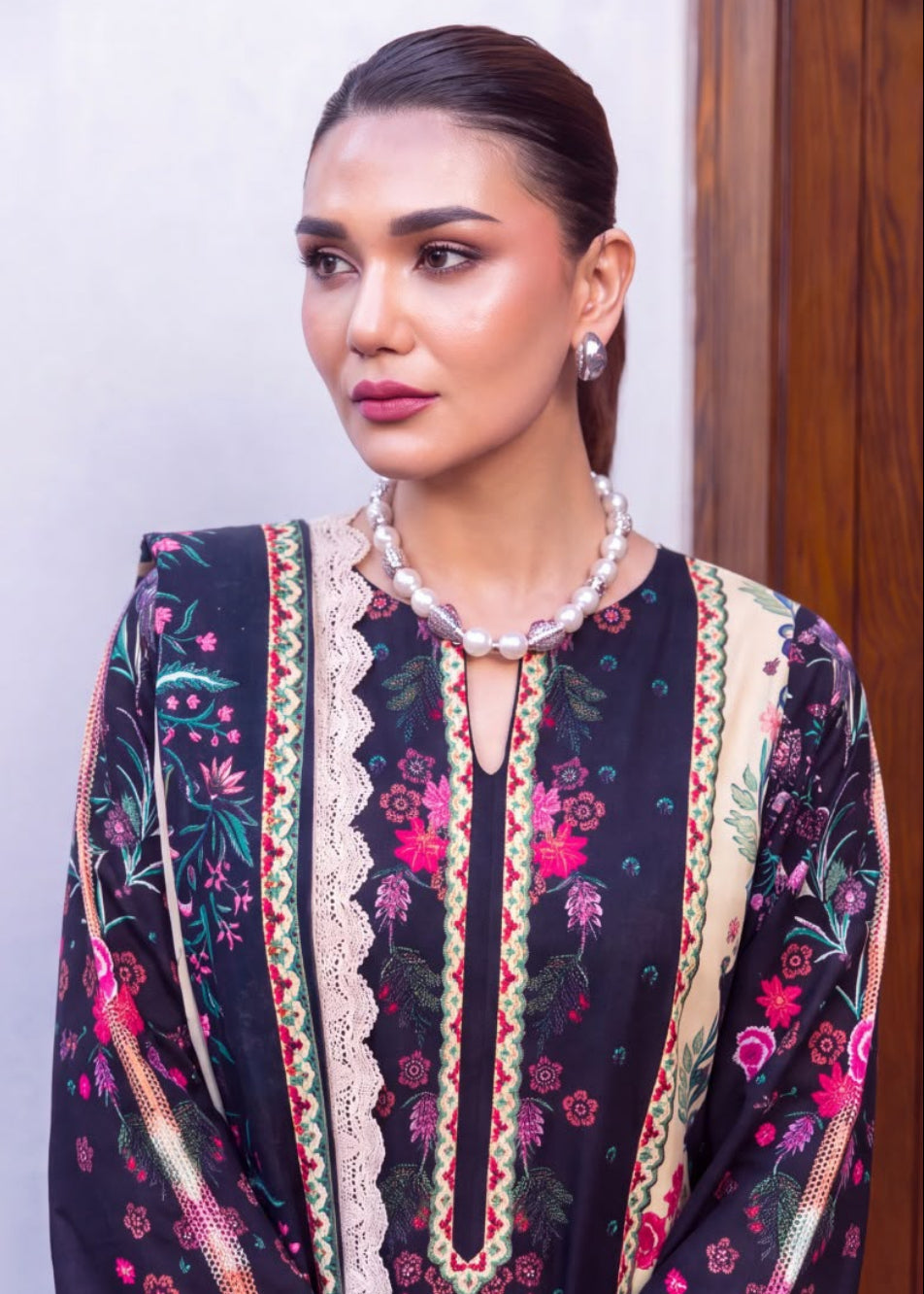 A model is shown wearing a traditional South Asian salwar kameez suit in a split-screen format, featuring a full-length seated view on the left and a close-up of the chest and neckline on the right. The outfit consists of a black base with intricate floral embroidery in pink, red, and green, accented by beige lace borders and a matching dupatta.