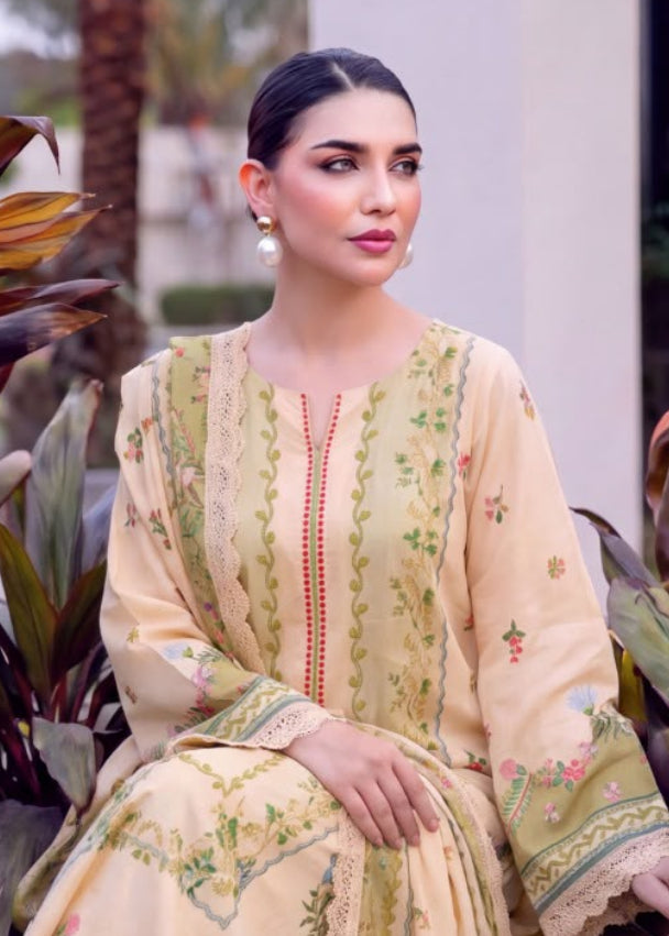 A woman modeling a traditional embroidered outfit in an outdoor setting with plants. The outfit is a light beige three-piece set with green floral embroidery and a matching green dupatta.