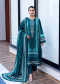 A woman models a traditional South Asian salwar kameez suit in deep teal green with intricate silver embroidery, paired with matching trousers and a coordinating dupatta, set against a modern interior background with large windows.