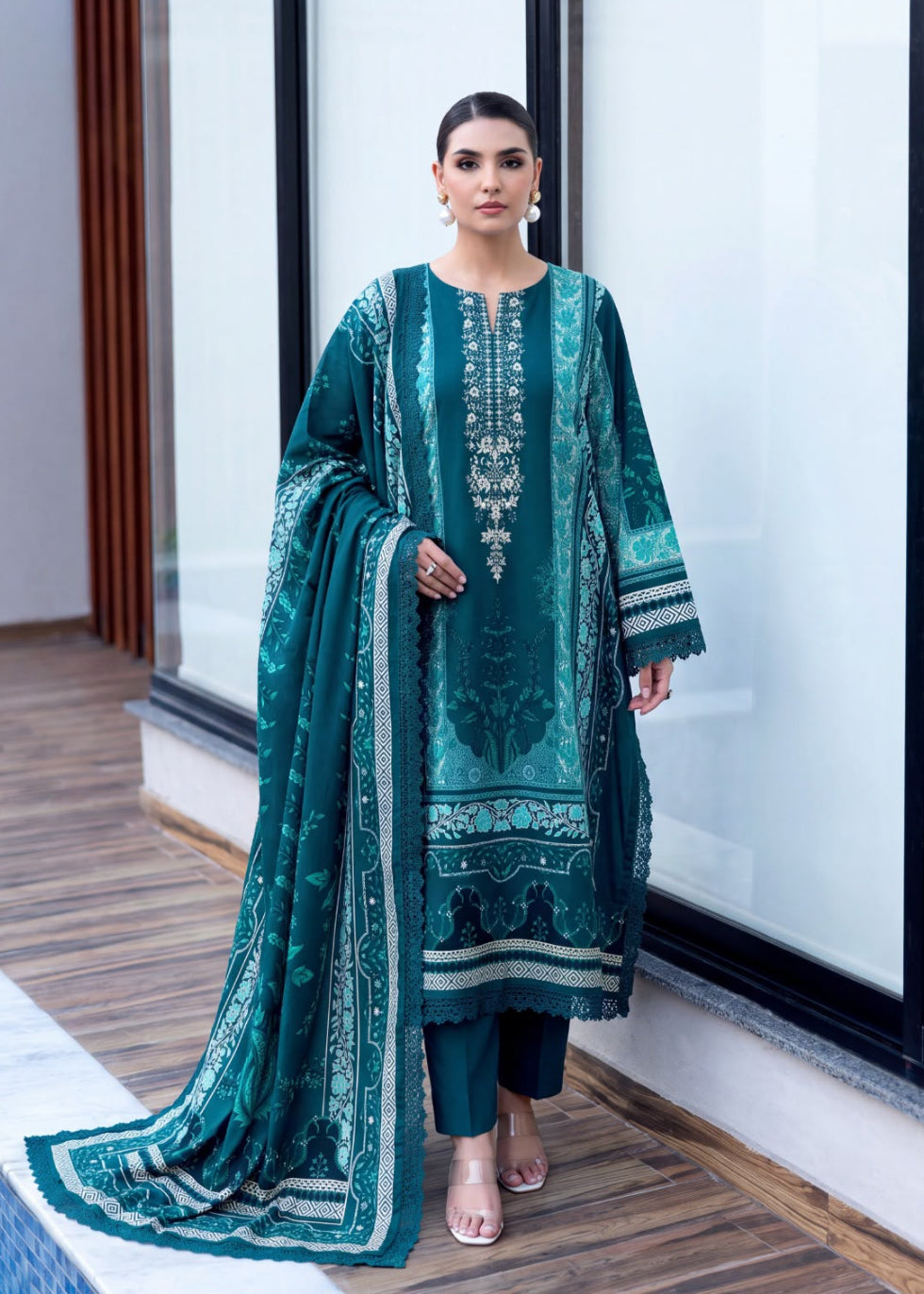 A woman models a traditional South Asian salwar kameez suit in deep teal green with intricate silver embroidery, paired with matching trousers and a coordinating dupatta, set against a modern interior background with large windows.