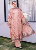 A woman models a traditional three-piece salwar kameez suit in dusty pink, featuring intricate floral embroidery in red, green, and gold, paired with matching wide-leg trousers and a dupatta, set against an outdoor backdrop of a white wall and green grass.