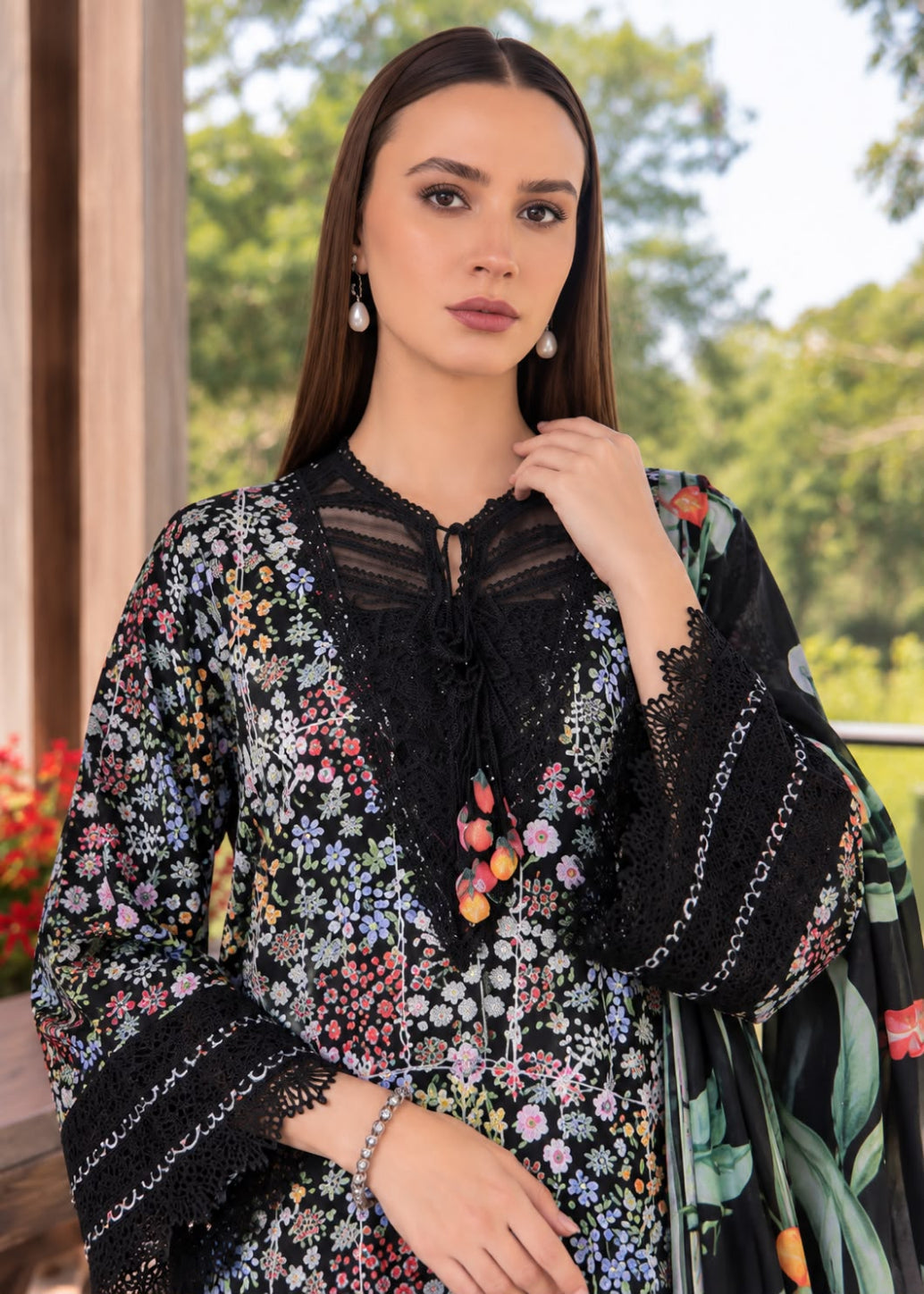 A woman modeling a black floral embroidered kurta with lace trim and a matching printed dupatta, set against an outdoor garden background.