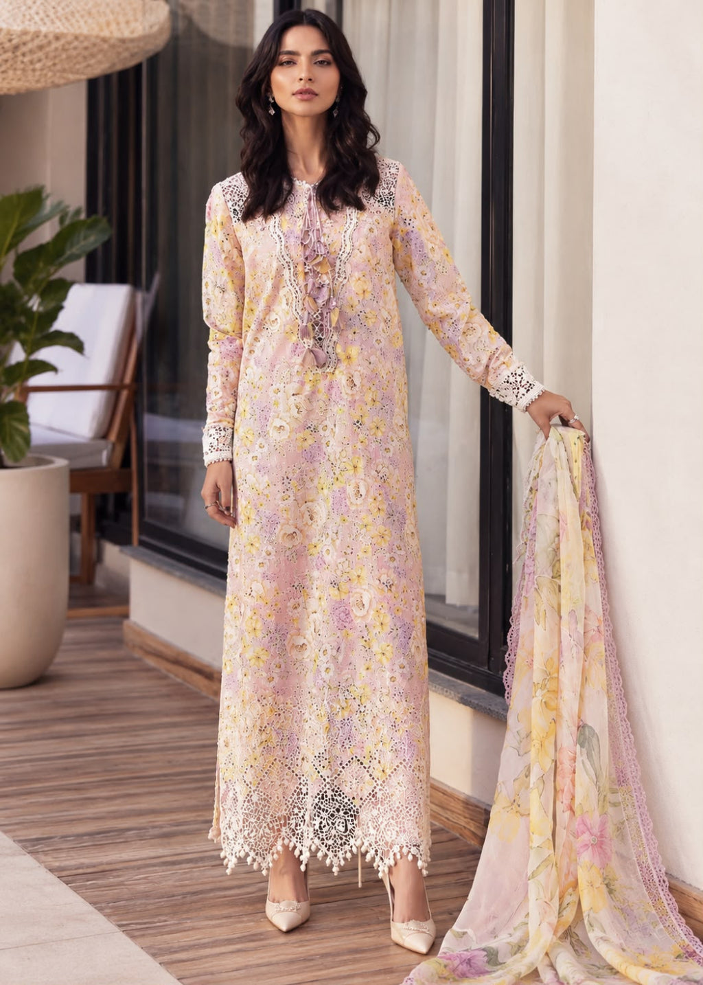 A woman models a traditional long kurta in a soft pastel floral print with matching embroidered dupatta in an outdoor patio setting.